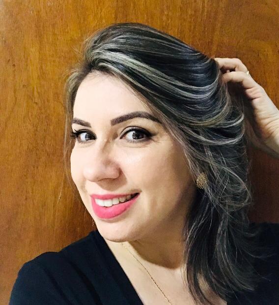 Sorridente com batom rosa e diante de uma parede de madeira, Vanessa toca os cabelos mesclados de louro e castanho
